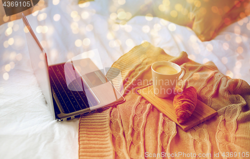 Image of laptop, coffee and croissant on bed at cozy home
