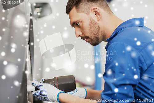 Image of auto mechanic with screwdriver changing car tire