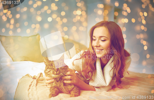 Image of happy young woman with cat lying in bed at home