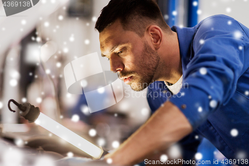 Image of mechanic man with lamp repairing car at workshop