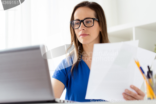 Image of businesswoman with papers and laptop at office