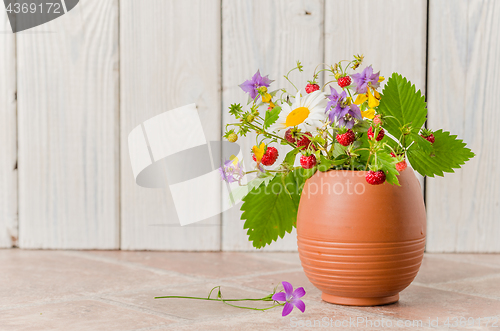 Image of Ripe strawberries and a bouquet of forest flowers in a clay mug