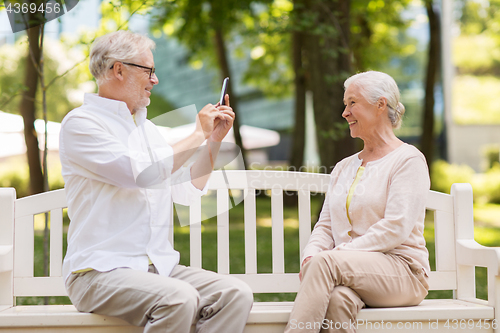 Image of old woman photographing man by smartphone in park