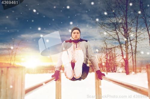 Image of young man exercising on parallel bars in winter