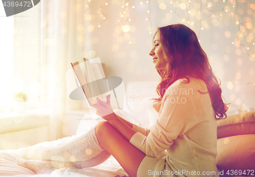 Image of happy young woman reading book in bed at home