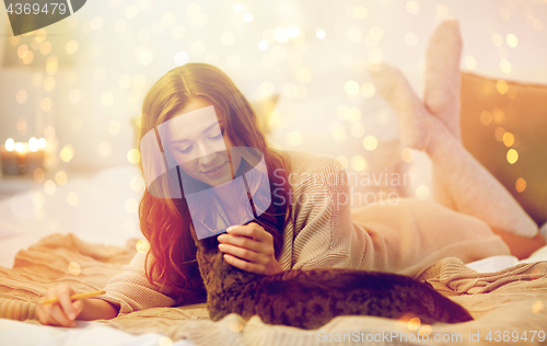 Image of happy young woman with cat lying in bed at home