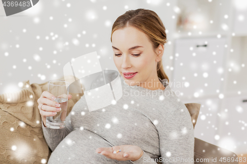 Image of happy pregnant woman with water and pills at home