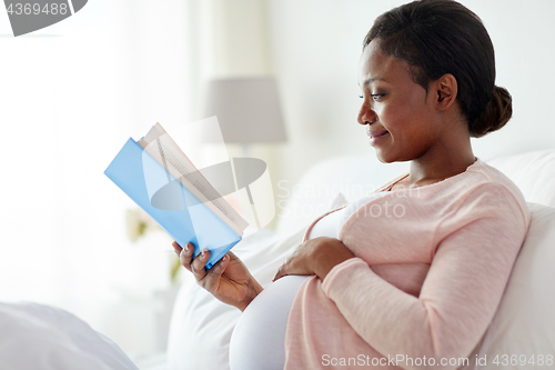 Image of happy pregnant african woman reading book at home