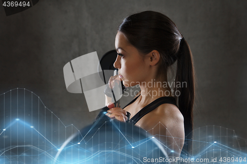 Image of young woman flexing muscles with barbell in gym