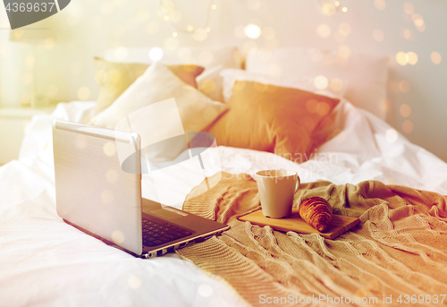 Image of laptop, coffee and croissant on bed at cozy home