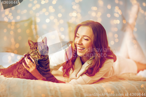 Image of happy young woman with cat lying in bed at home