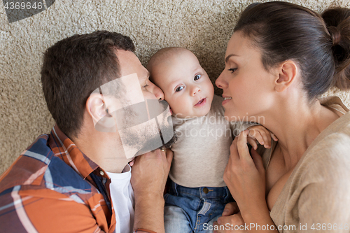 Image of happy family lying on floor and kissing their baby