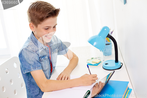 Image of student boy with tablet pc writing to notebook