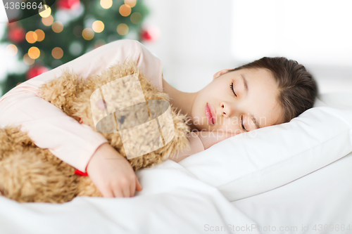 Image of girl sleeping with teddy bear in bed at christmas