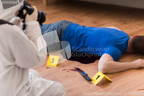 Image of criminalist photographing dead body at crime scene