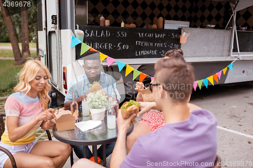 Image of happy friends with drinks eating at food truck