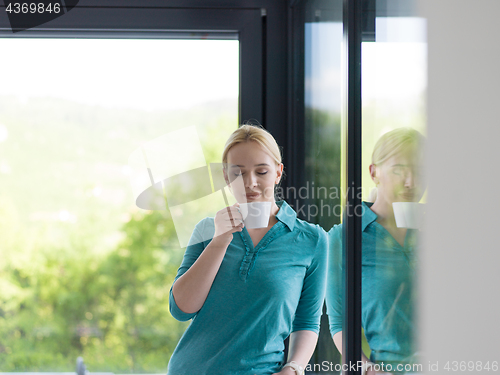 Image of young woman drinking morning coffee by the window