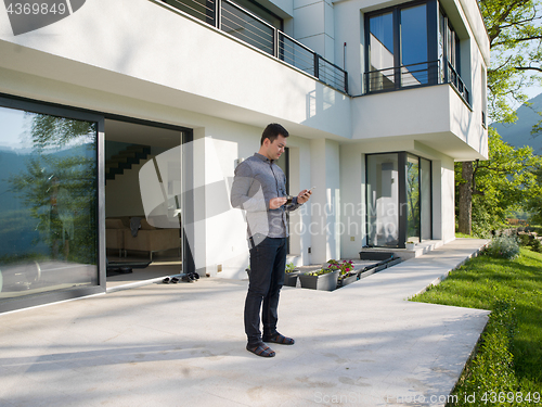 Image of man using mobile phone in front of his luxury home villa