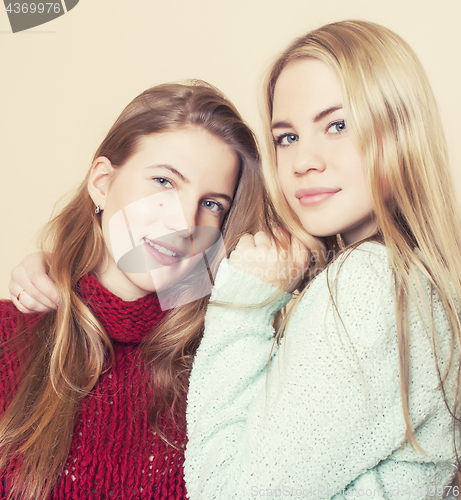 Image of Two young girlfriends in winter sweaters indoors having fun. Lifestyle. Blond teen friends close up