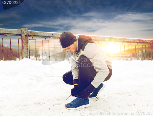 Image of man with earphones tying sports shoes in winter