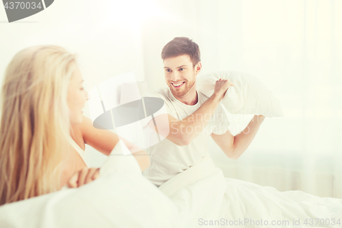 Image of happy couple having pillow fight in bed at home