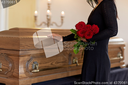 Image of sad woman with red roses and coffin at funeral