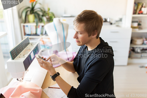 Image of fashion designer with smartphone working at studio