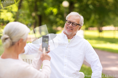 Image of old woman photographing man by smartphone in park