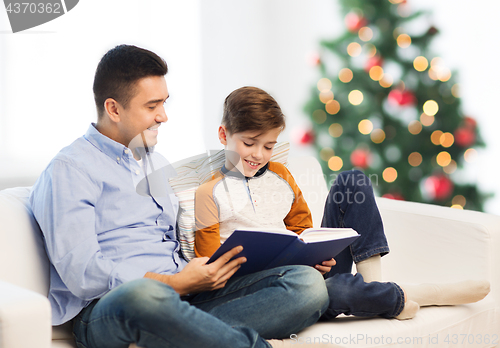 Image of happy father and son reading book at christmas