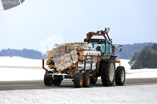 Image of Farm Tractor Transports Logs on Wood Trailer