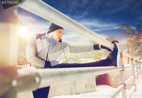 Image of sports man stretching leg at fence in winter