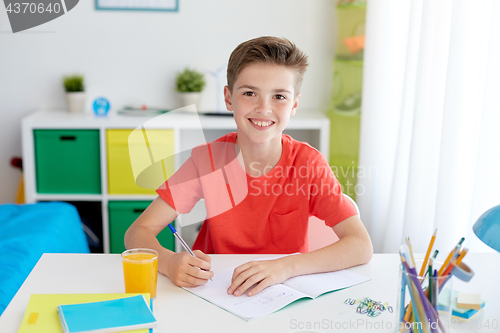 Image of happy student boy writing to notebook at home