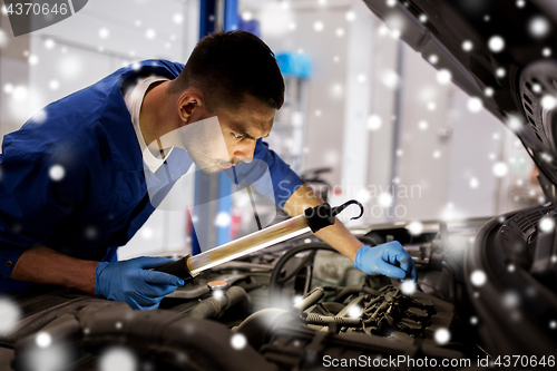 Image of mechanic man with lamp repairing car at workshop