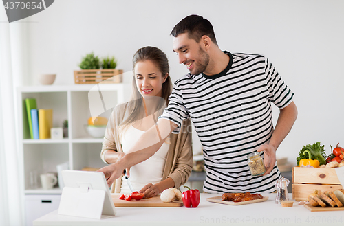 Image of happy couple with tablet pc cooking food at home