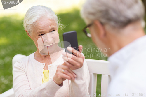 Image of old woman photographing man by smartphone in park