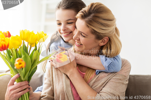 Image of happy girl giving flowers to mother at home