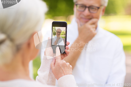 Image of old woman photographing man by smartphone in park