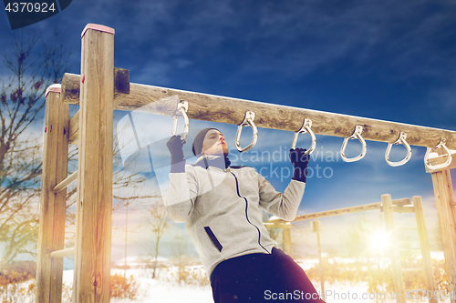 Image of young man exercising on horizontal bar in winter