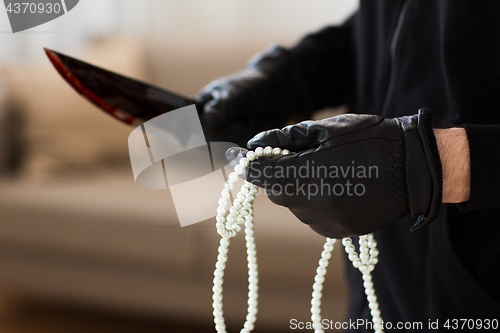 Image of criminal with knife and jewelry at crime scene