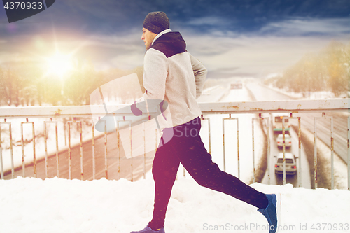 Image of man running along snow covered winter bridge road