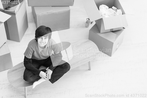 Image of boy sitting on the table with cardboard boxes around him top vie