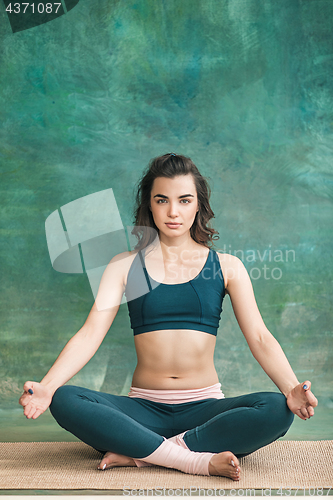 Image of Studio shot of a young woman doing yoga exercises on green background