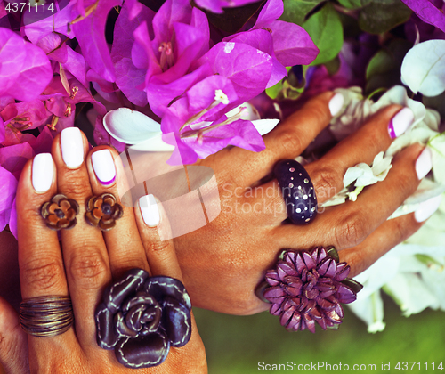 Image of bright colorfull shot of african tanned hands with manicure among pink flowers wearing jewellery 