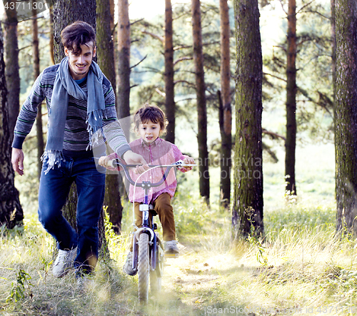 Image of father learning his son to ride on bicycle outside in park