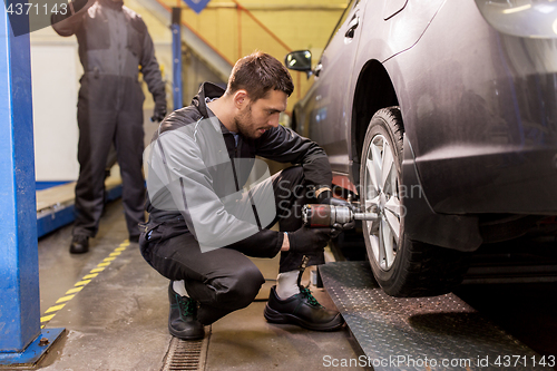 Image of auto mechanic with screwdriver changing car tire