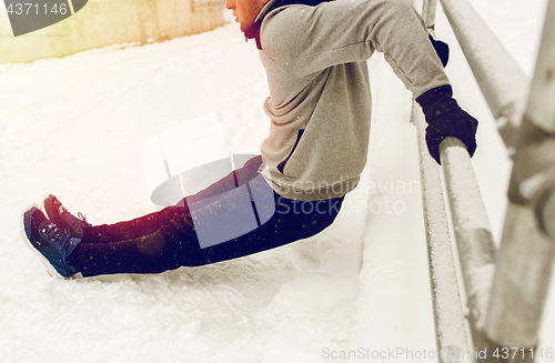 Image of sports man doing triceps dips at fence in winter