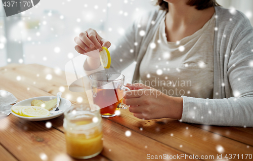 Image of close up of woman adding honey to tea with lemon