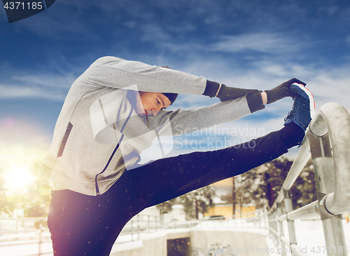 Image of sports man stretching leg at fence in winter