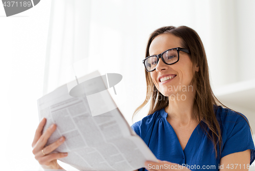 Image of happy woman in glasses reading newspaper at office