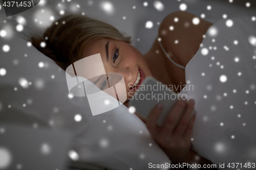 Image of young woman with smartphone in bed at home bedroom